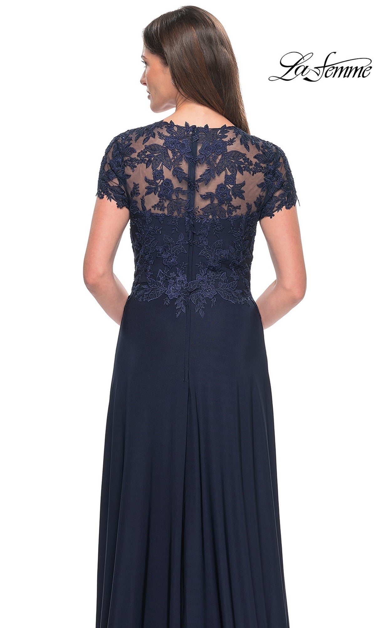 Woman wearing a La Femme Cap Sleeve Long Purple Prom Dress 31906, featuring navy blue lace detailing on the sheer back and short sleeves, facing away from the camera. “La Femme” logo appears in the top right corner.